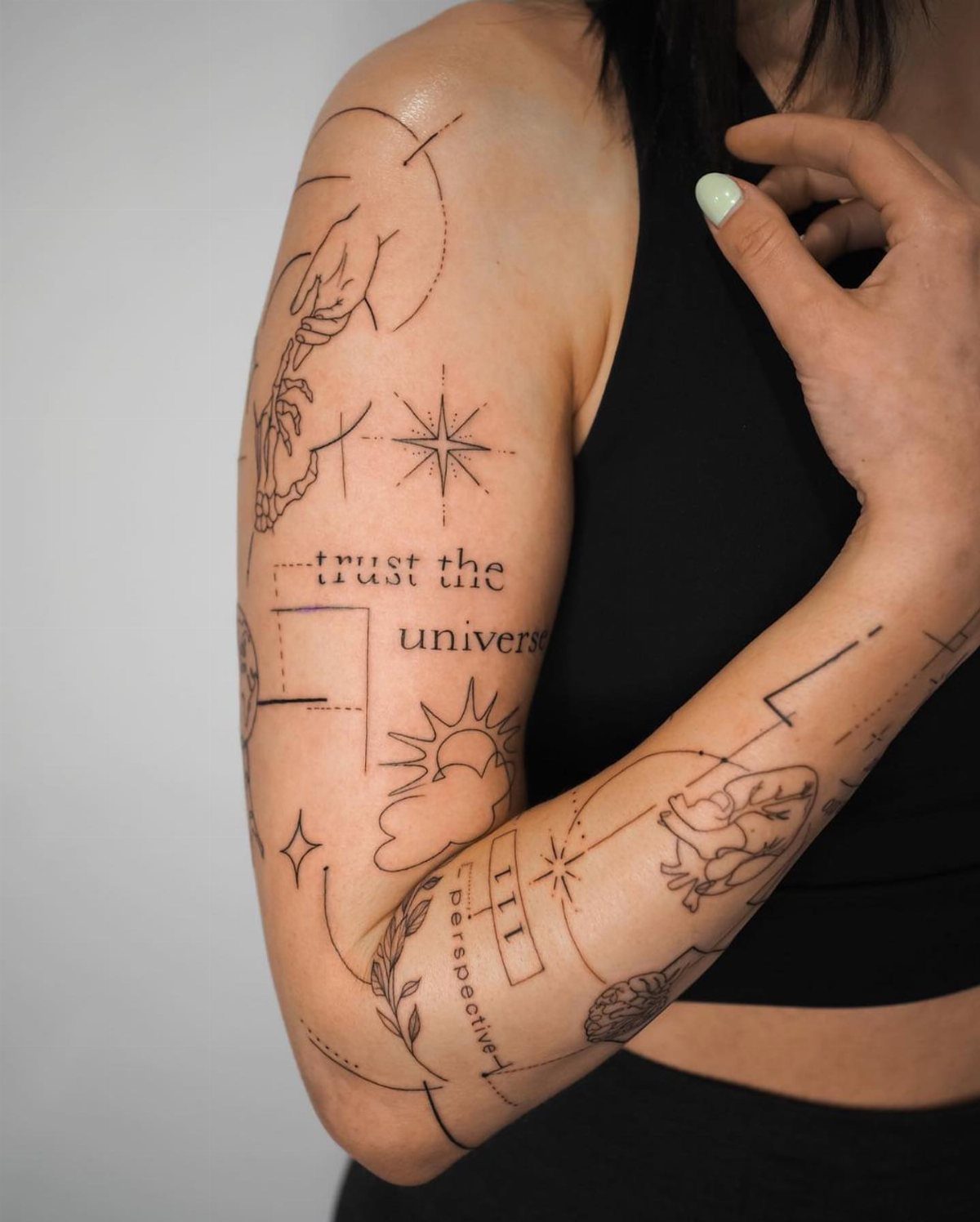 Minimalist line art tattoo on a forearm featuring celestial symbols and thin black lines.