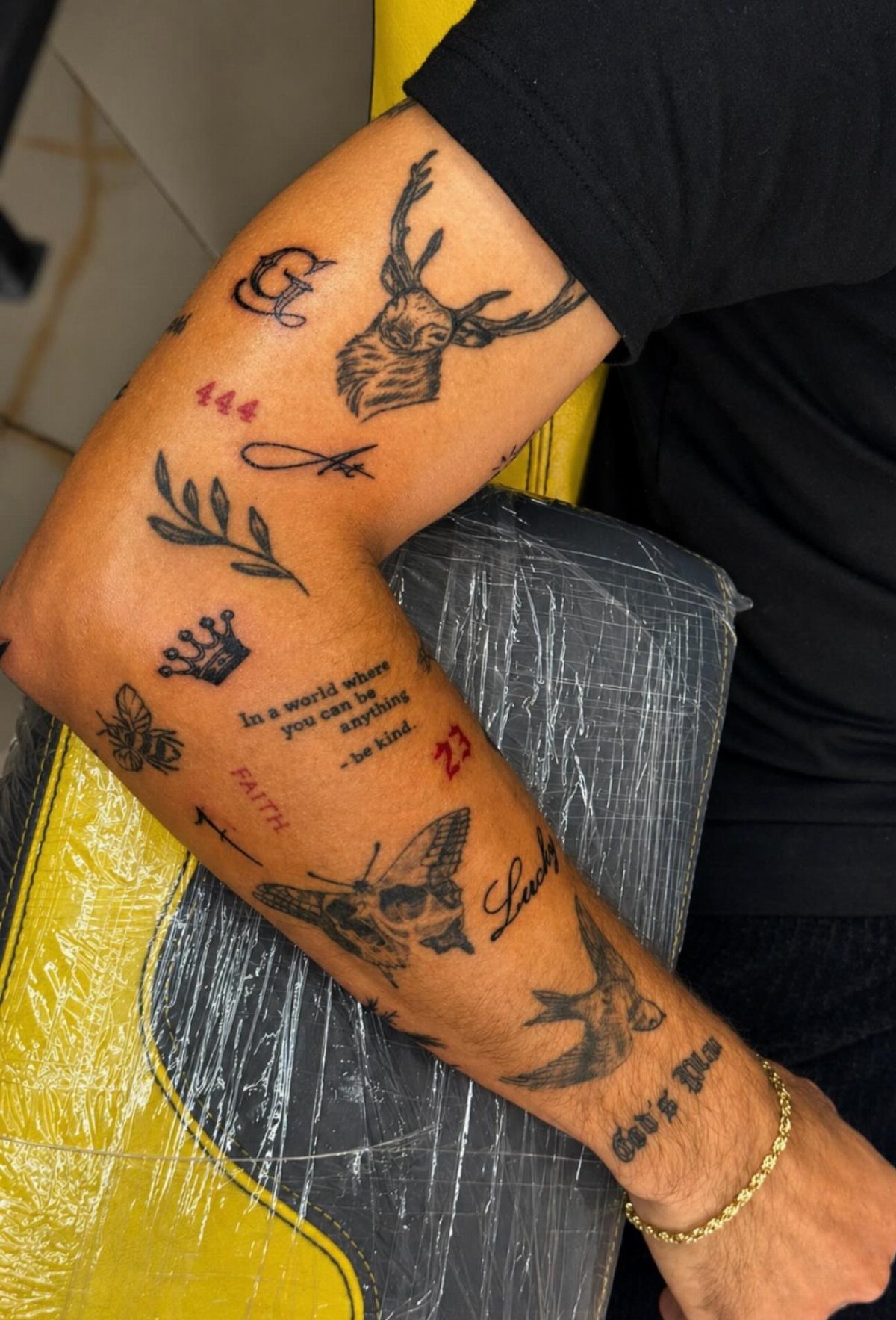 Forearm and upper arm with various small black ink tattoos including a deer and butterfly.