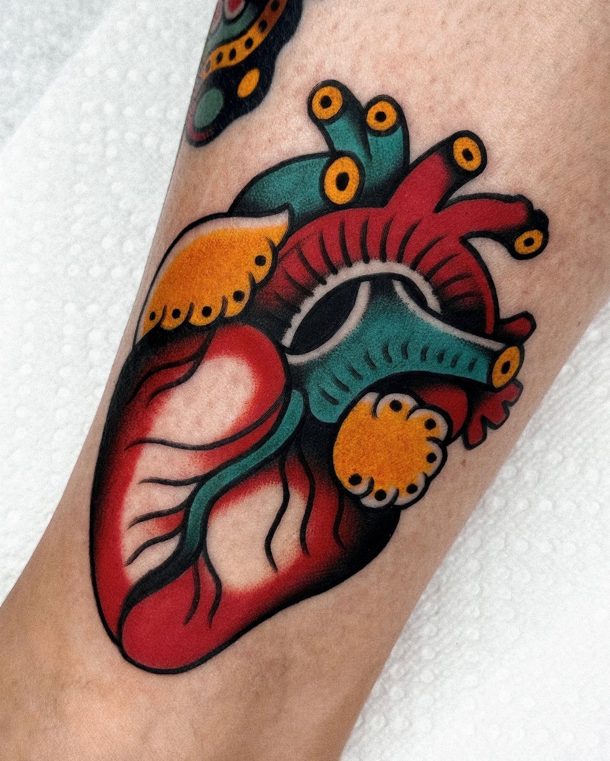 Anatomical heart tattoo with red, teal, and yellow colors on skin.