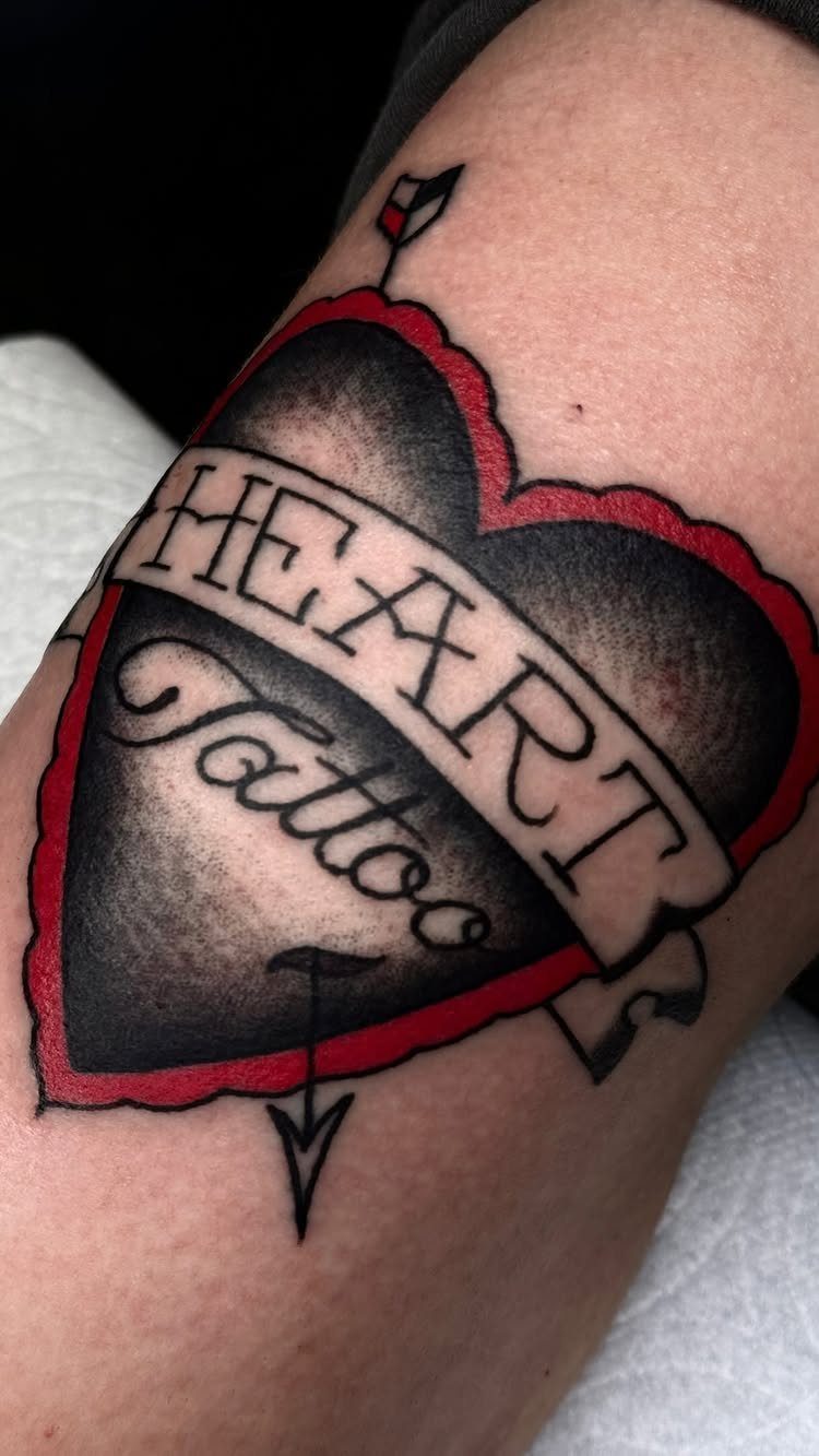 Black heart tattoo with red outline and arrow on a person's skin