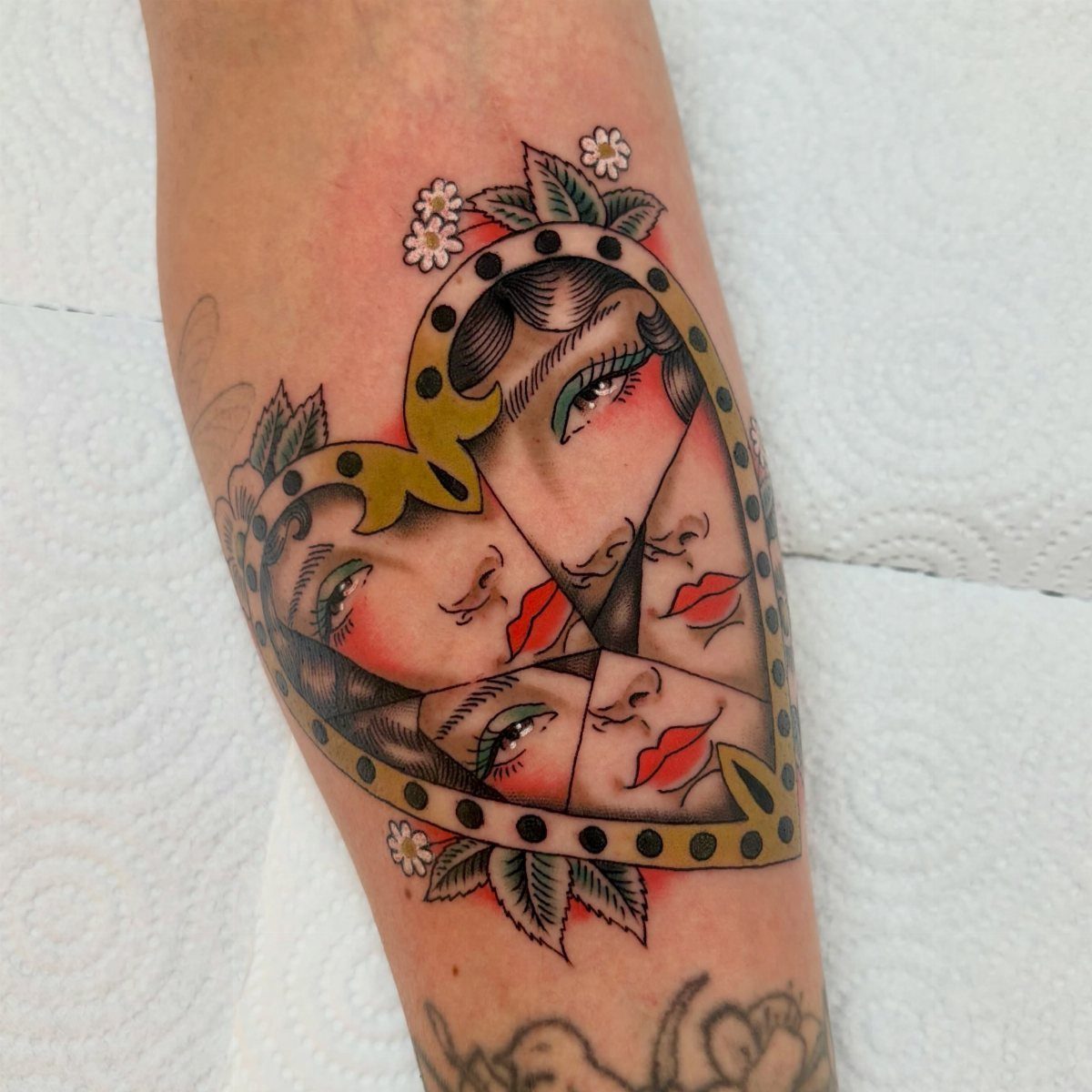 Heart-shaped broken mirror tattoo reflecting a woman's face with red lips and floral accents.