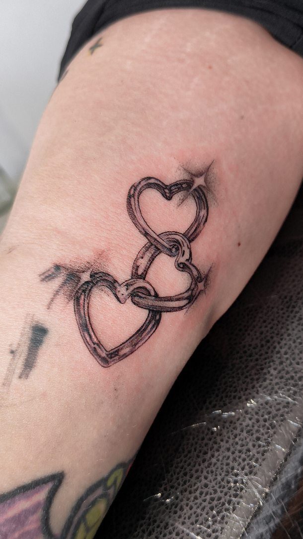 Interlocking chain link heart tattoo in black and grey ink on skin.