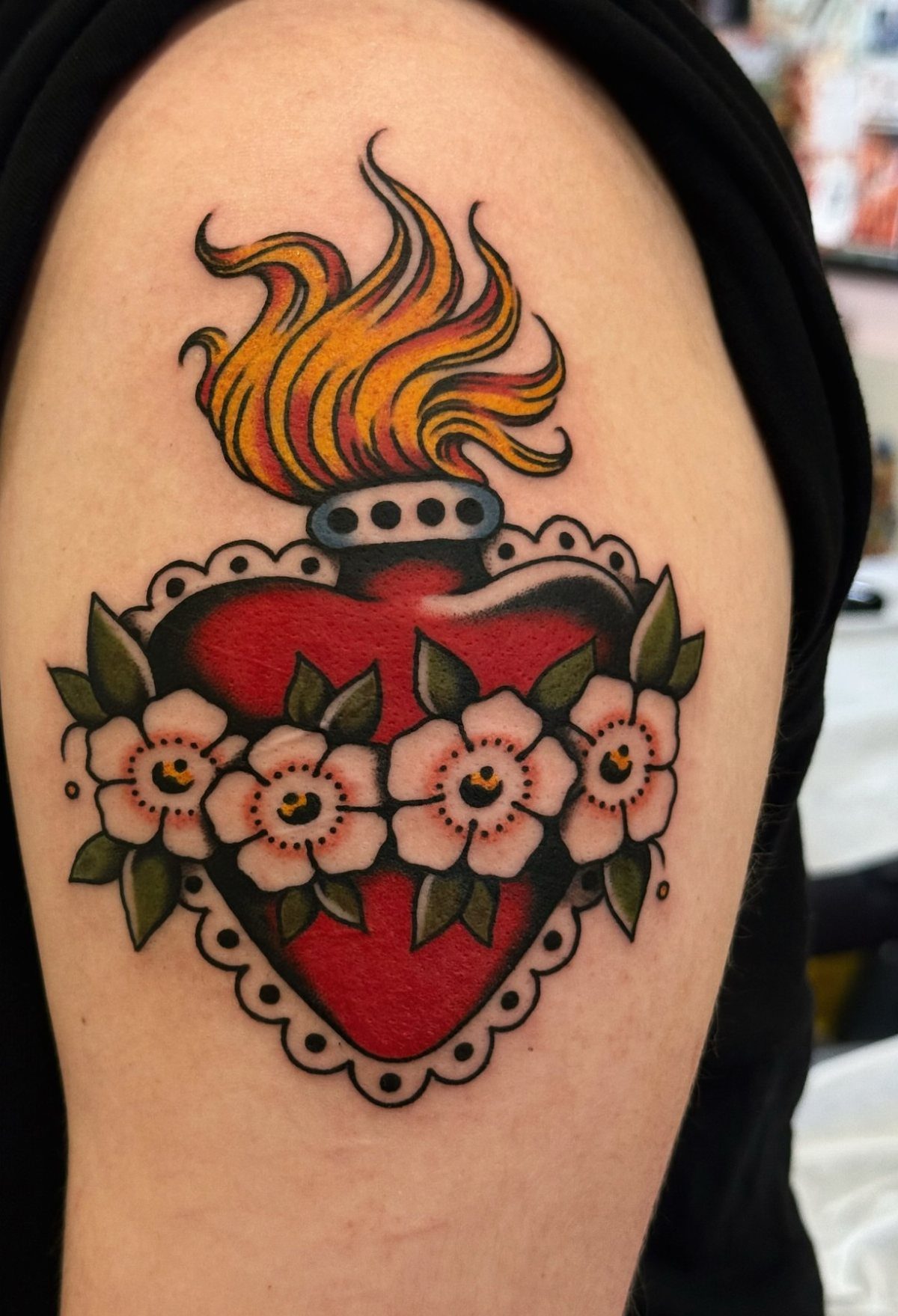Traditional red heart tattoo with flames and white flowers on an upper arm.