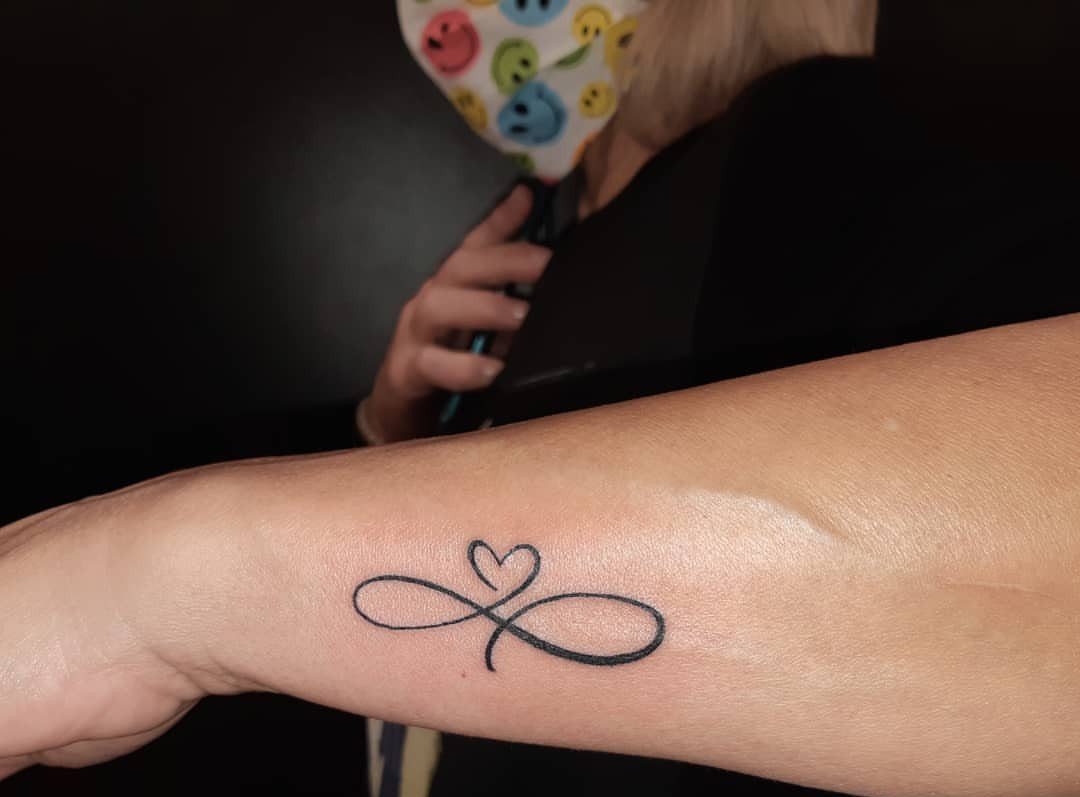 Infinity symbol tattoo with a heart in the center on a person's wrist