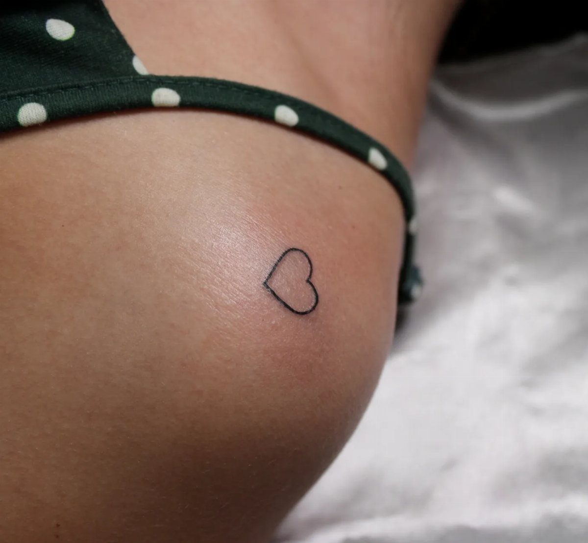 Small black heart outline tattoo on a person's hip near a green bikini.