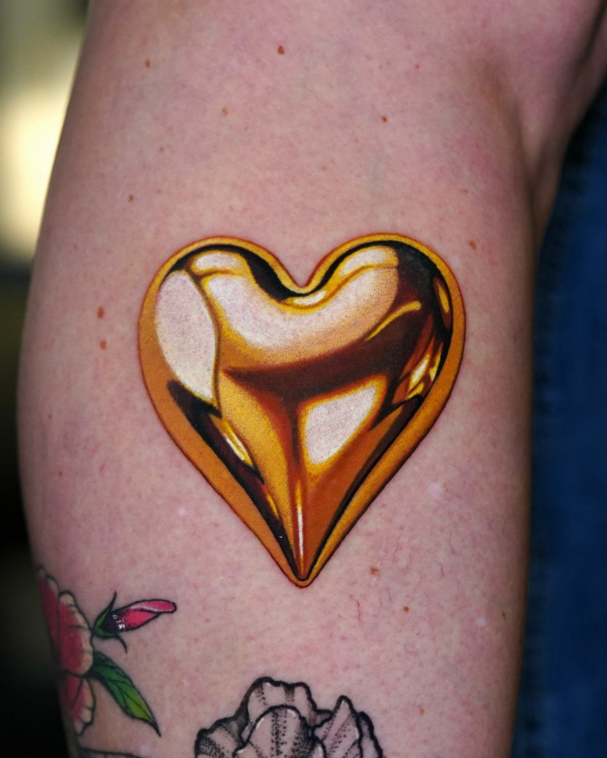 Shiny metallic gold heart tattoo on a person's arm with realistic 3D reflections.