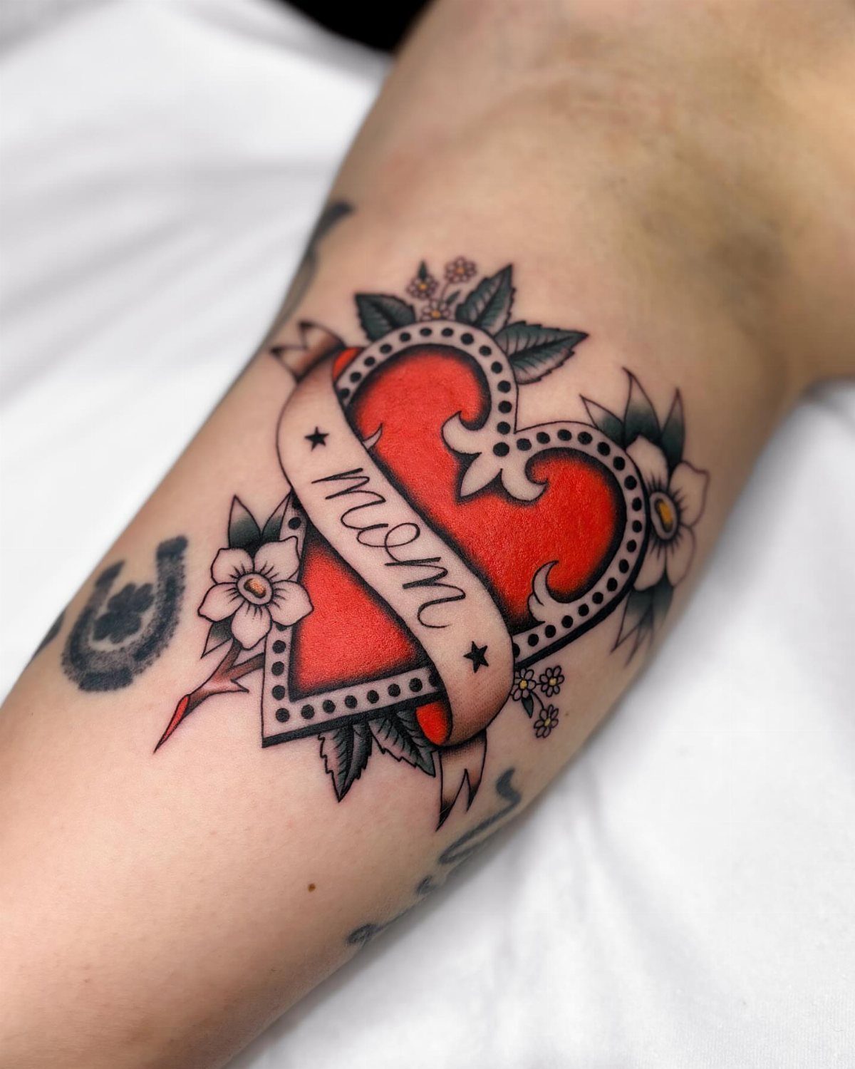 Traditional red heart tattoo with a mom banner and flowers on skin.