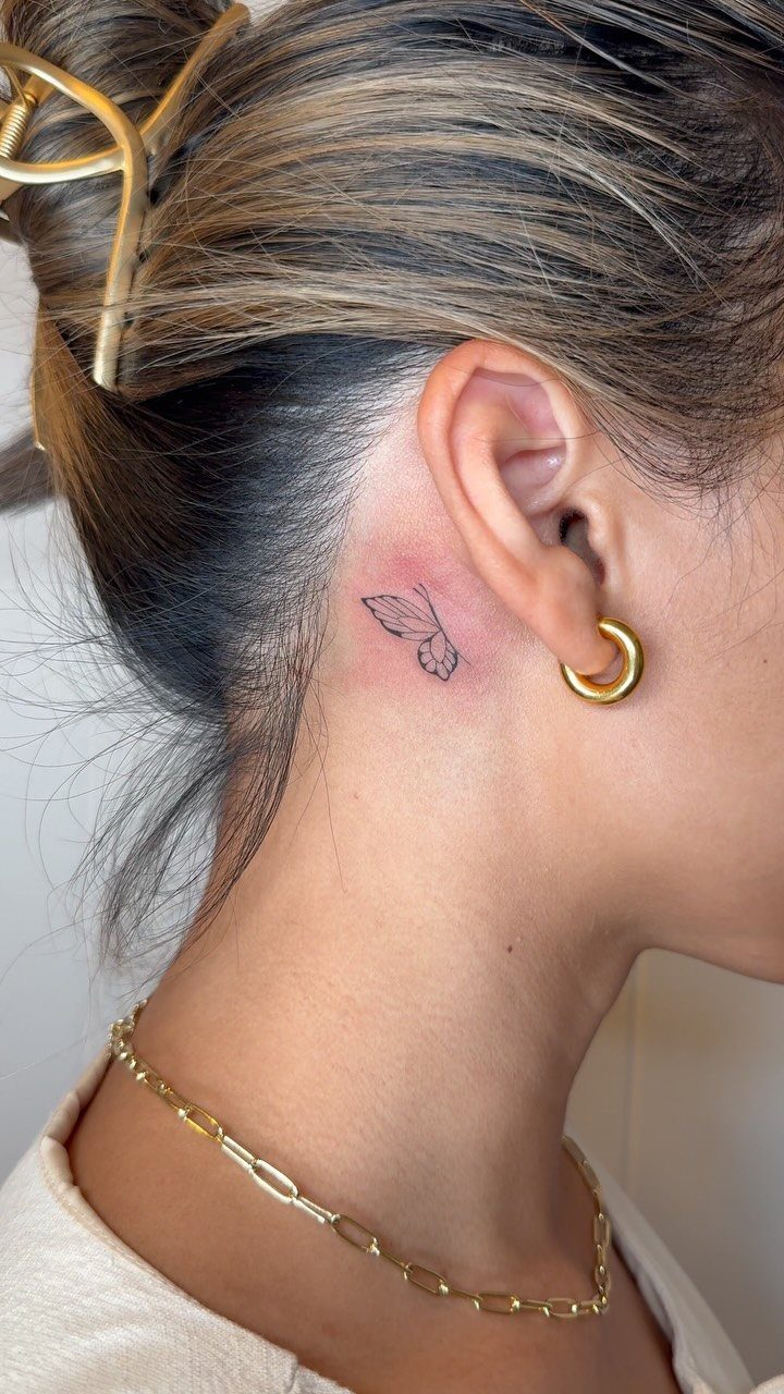 Small minimalist leaf line tattoo on a woman's neck behind her ear.