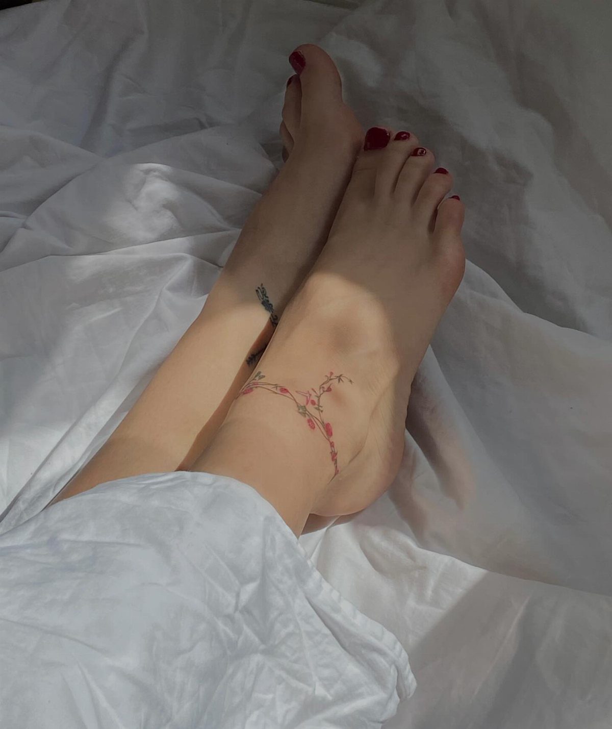 Feet on white sheets featuring a delicate floral tattoo wrapping around the ankle.