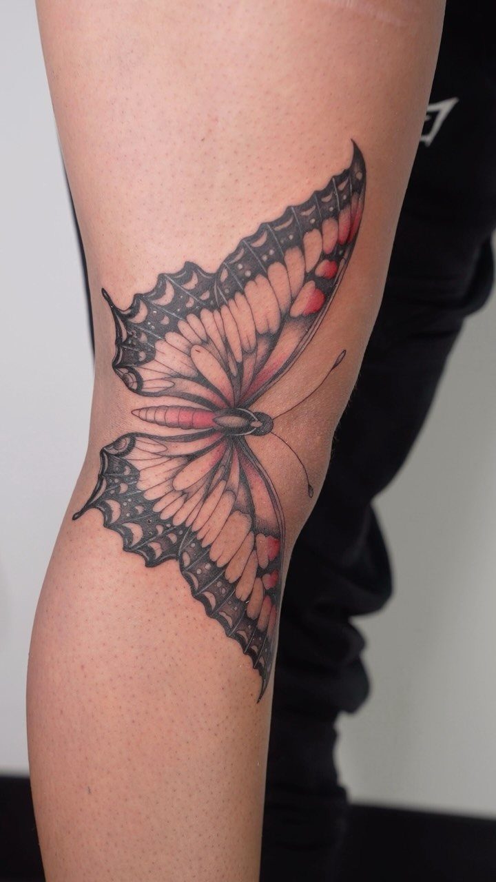 Butterfly tattoo with red and black ink on a person's leg.