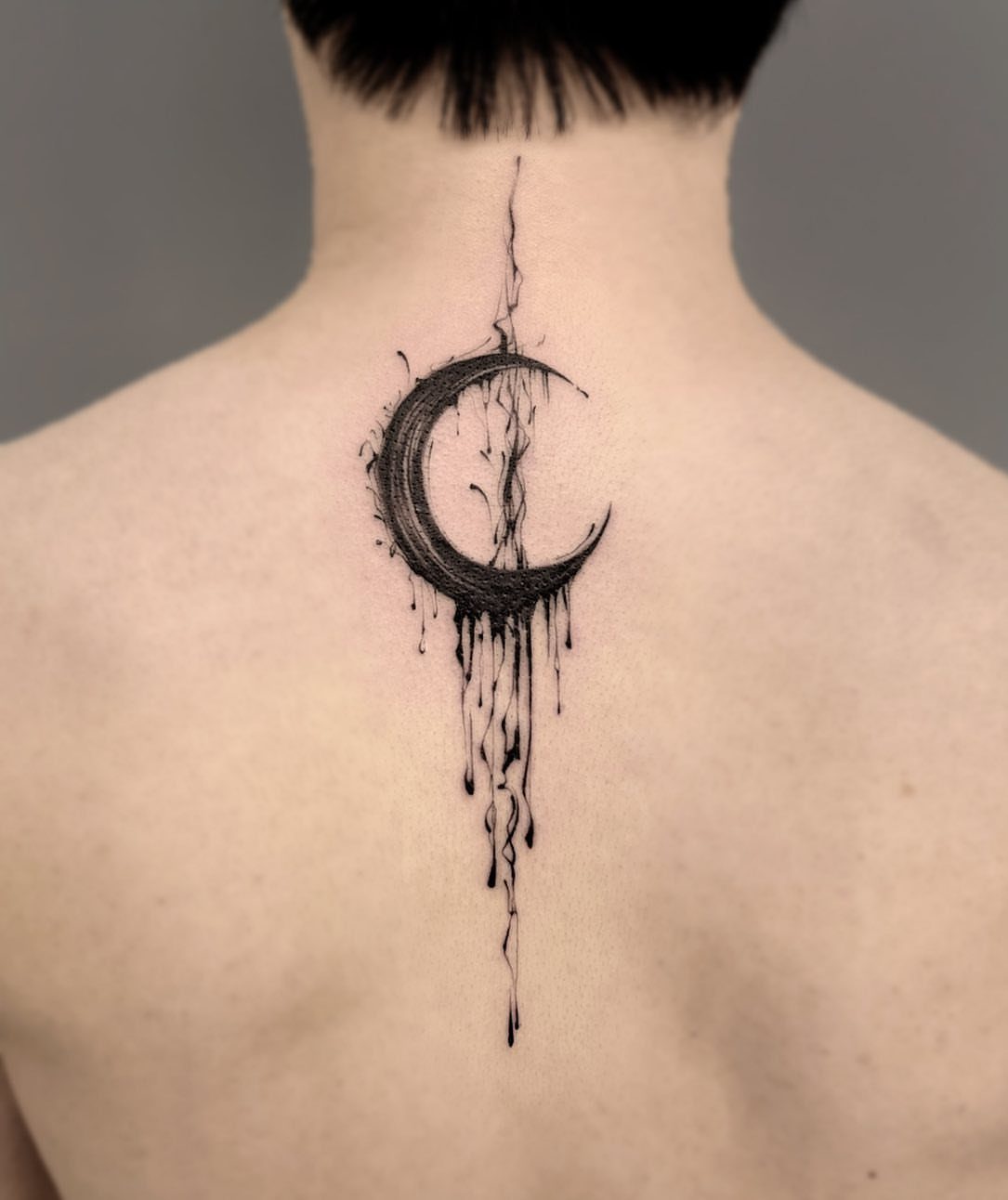 Crescent moon tattoo with dripping ink on the back of a person's neck.