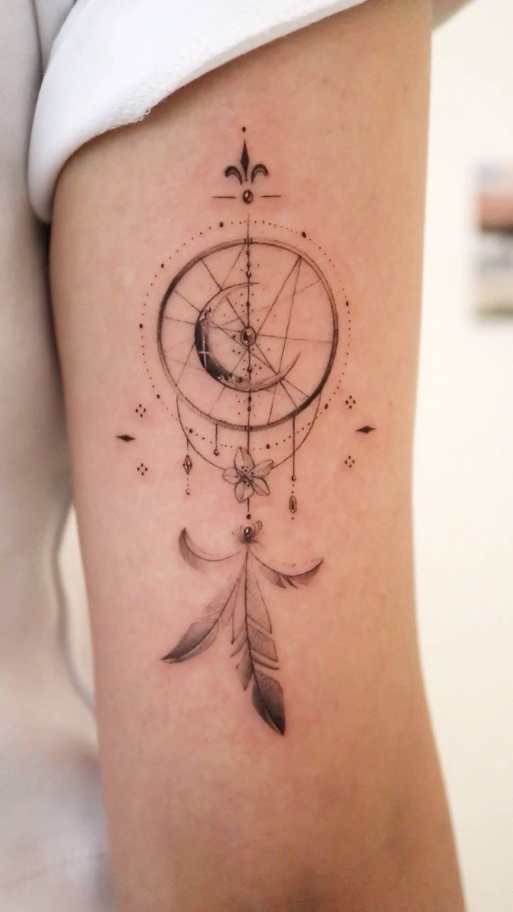 Geometric tattoo on an arm featuring a crescent moon and hanging feathers.