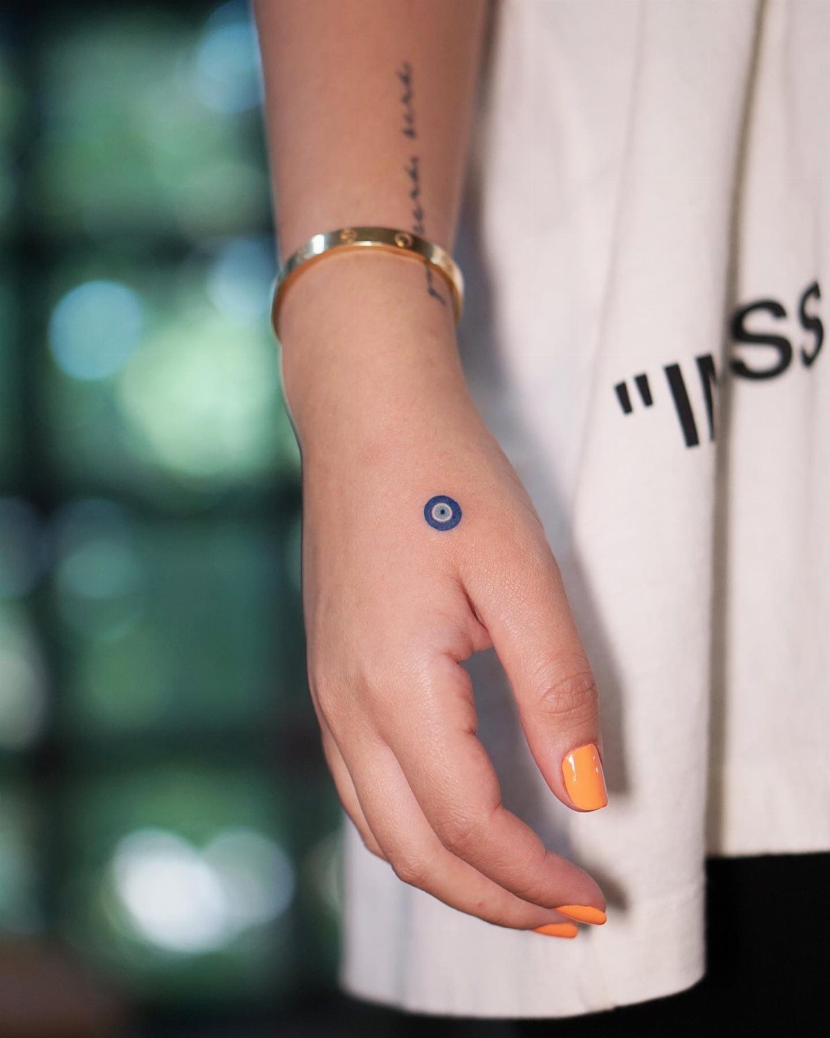 Small blue and white evil eye tattoo on the back of a hand
