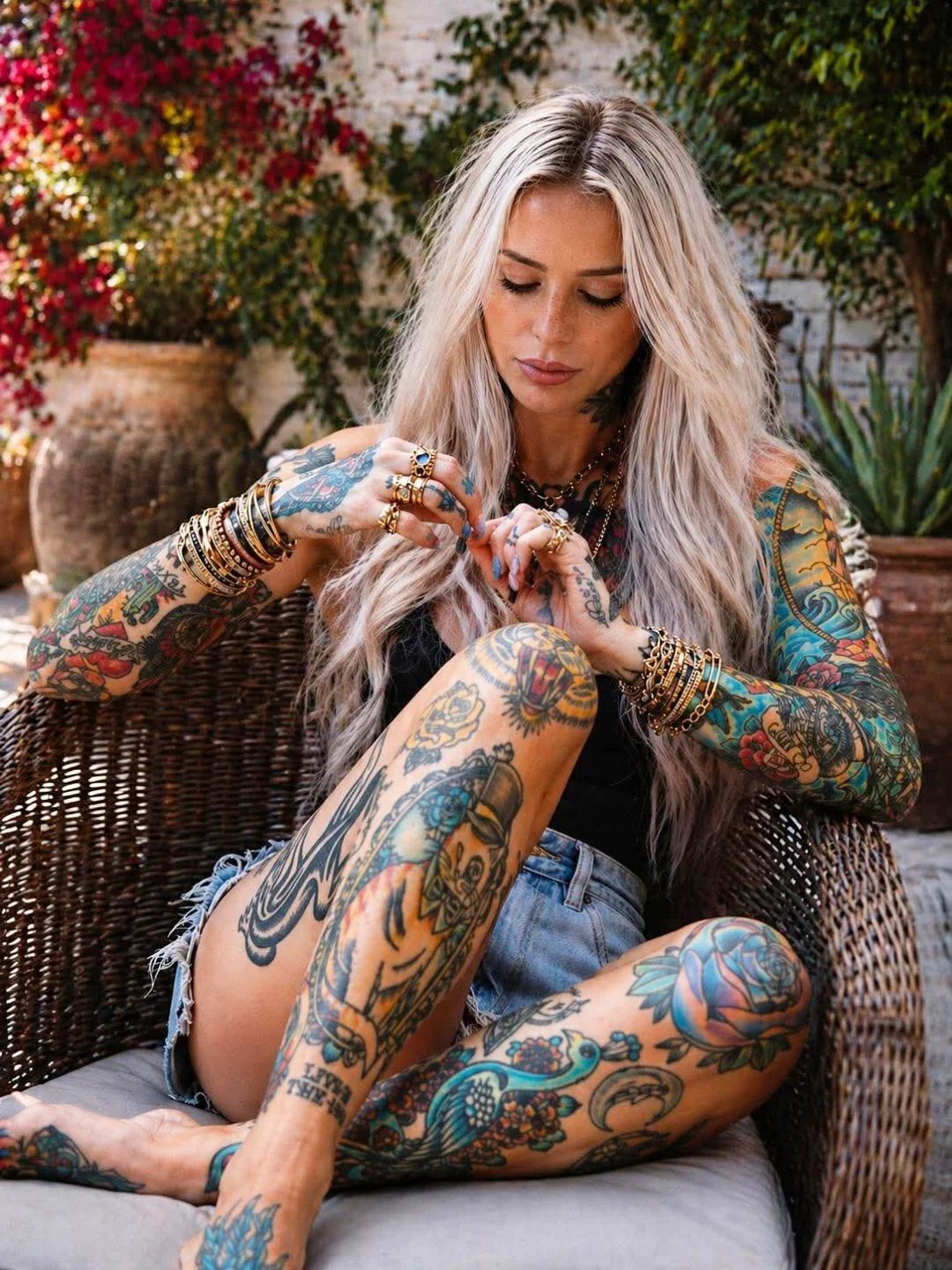 Woman with colorful full-body tattoos sitting in a wicker chair outdoors.