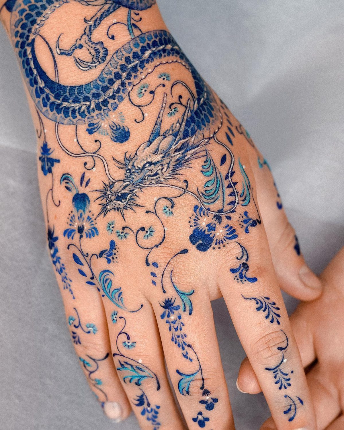 Blue dragon and floral tattoo covering a person's hand and wrist