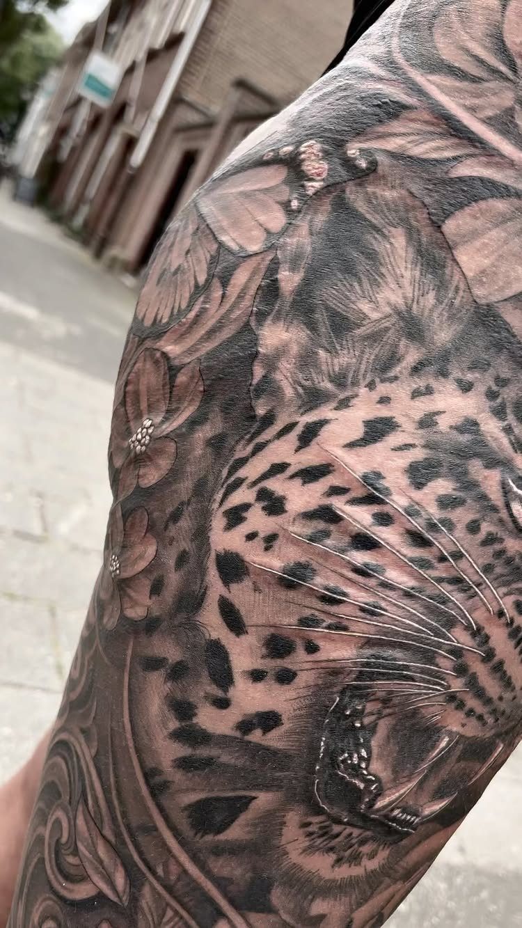 Detailed black and grey leopard tattoo with flowers on a person's shoulder and arm.