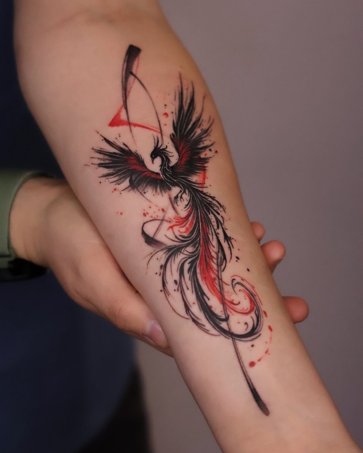 Phoenix tattoo with black and red ink on a person's forearm