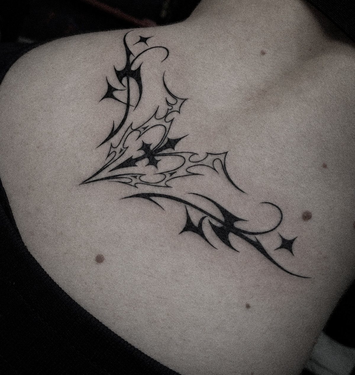 Tribal black ink tattoo with sharp curves and stars on a person's shoulder.