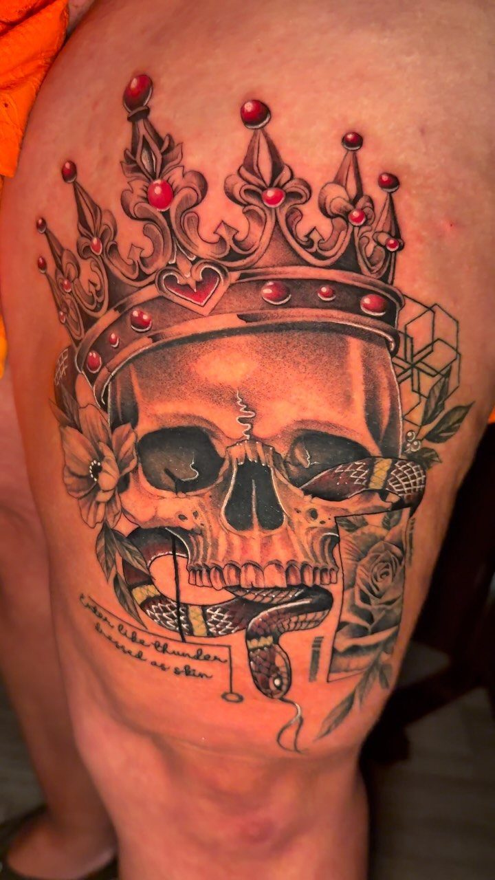 Skull tattoo with a red crown and snake on a person's thigh.