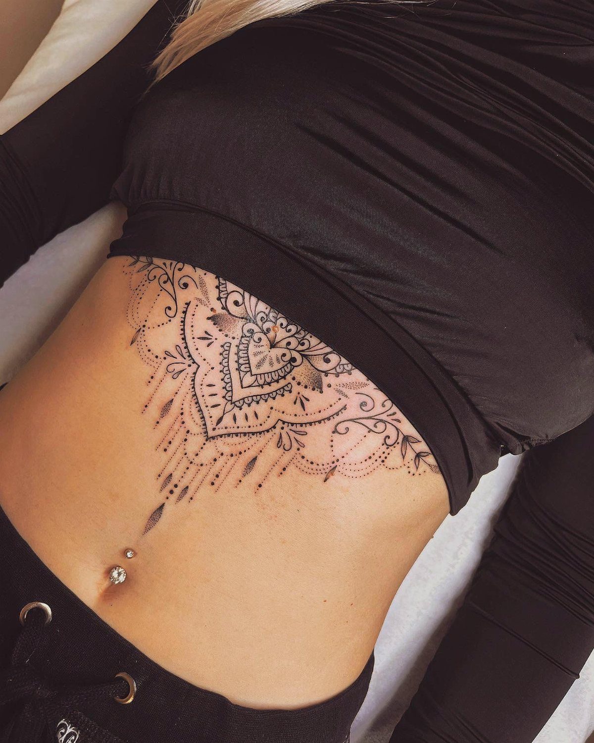 Intricate mandala tattoo on a woman's upper abdomen and ribcage under a black top