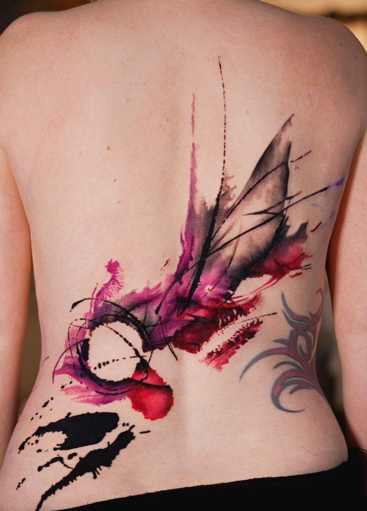 Abstract watercolor tattoo with pink and black ink splashes on a woman's back.