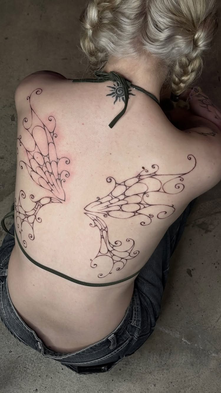 Stylized black ink wing tattoos on the back of a blonde woman