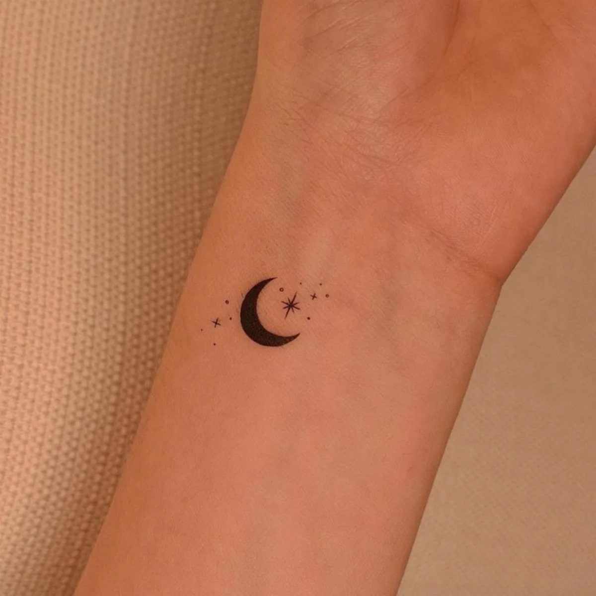 Crescent moon and stars tattoo on the inner wrist of a person.
