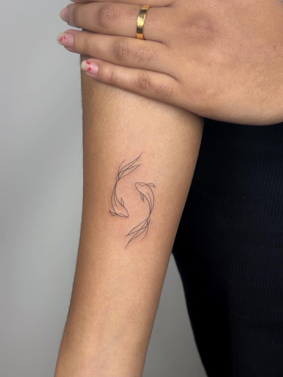 Two koi fish tattoo in a single continuous line on an inner forearm.