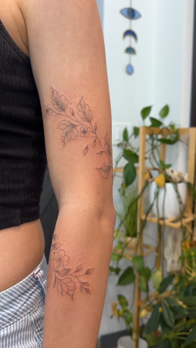 Fine-line floral tattoos with delicate leaves and blossoms on a person's inner arm.