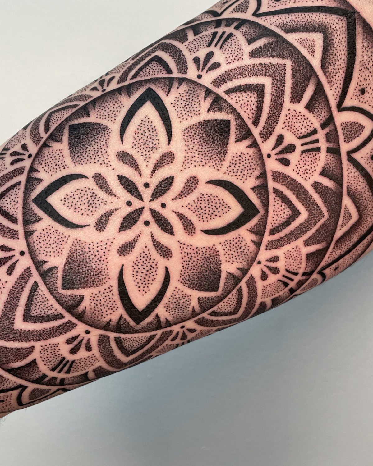 Geometric mandala tattoo with intricate dotwork on a person's inner arm.