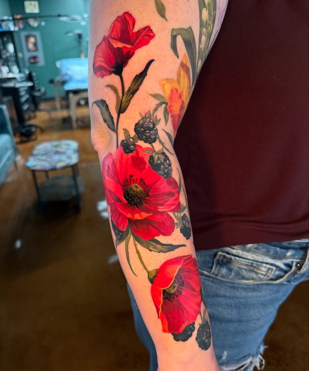 Colorful red poppy and berry tattoo on a person's inner forearm
