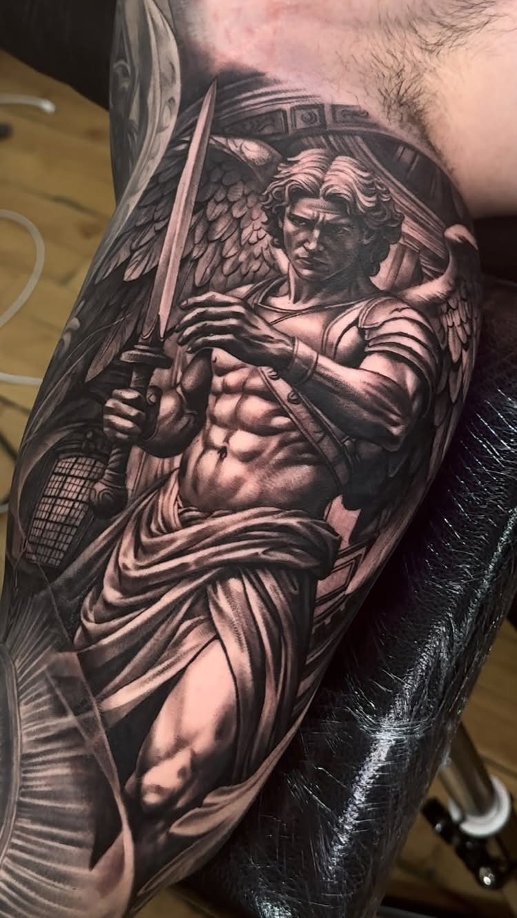 Muscular winged angel tattoo with a sword on a man's inner bicep.