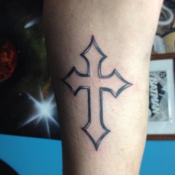 Stylized black ink cross tattoo on the inner bicep of a man's arm
