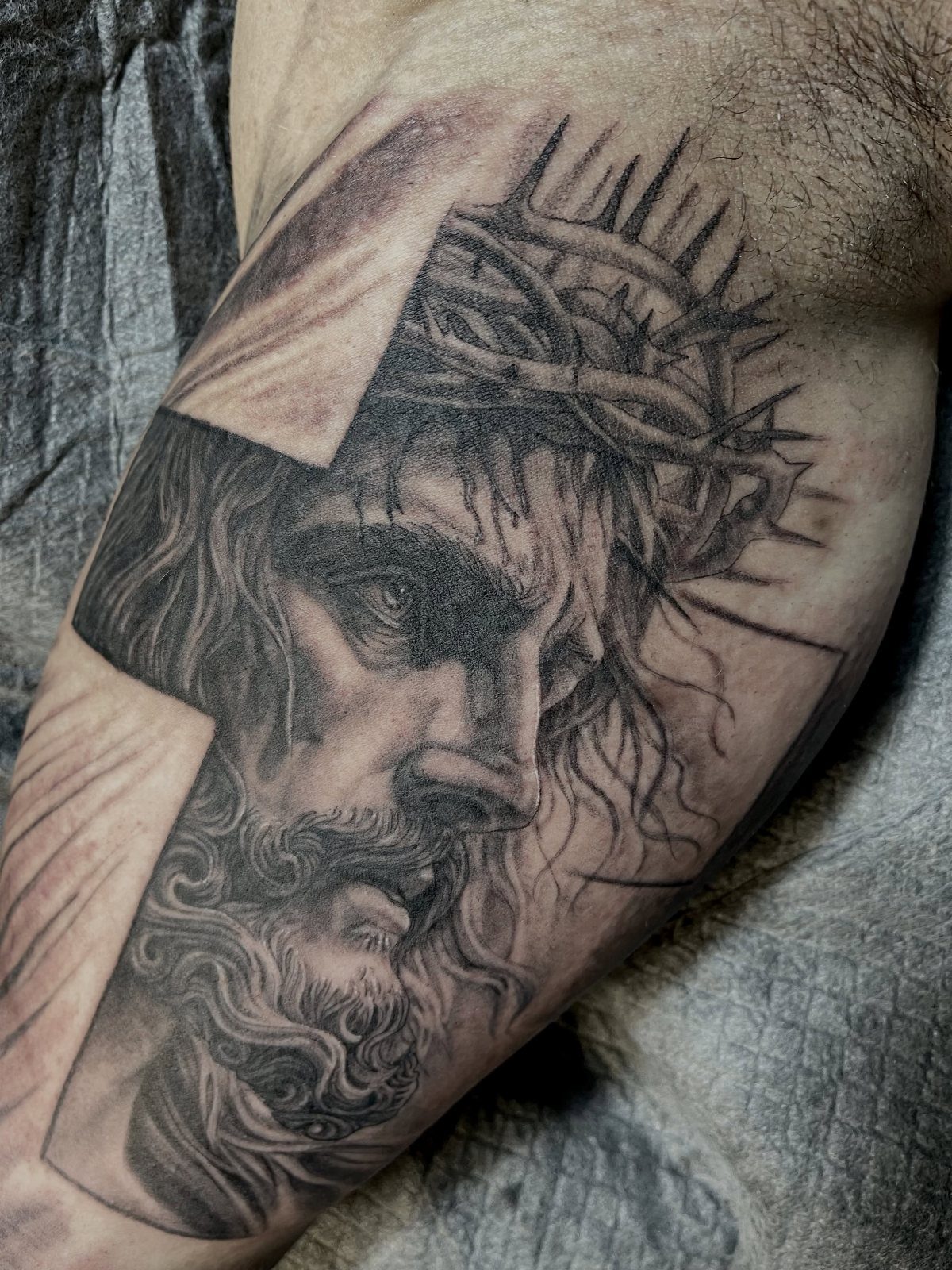 Jesus with crown of thorns tattoo on a man's inner bicep with cross background