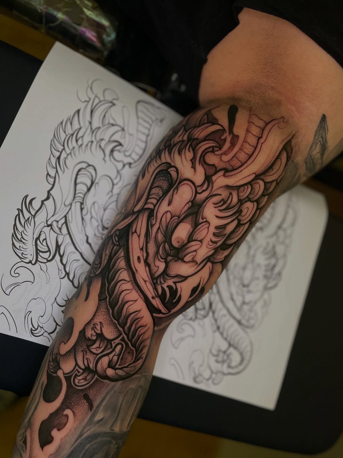 Dragon tattoo on a man's inner bicep next to a dragon drawing.