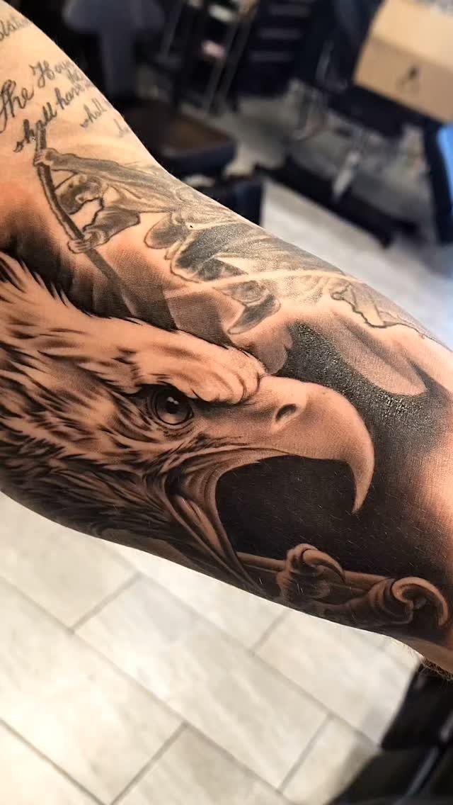 Eagle head tattoo in black and grey realism on a man's arm.