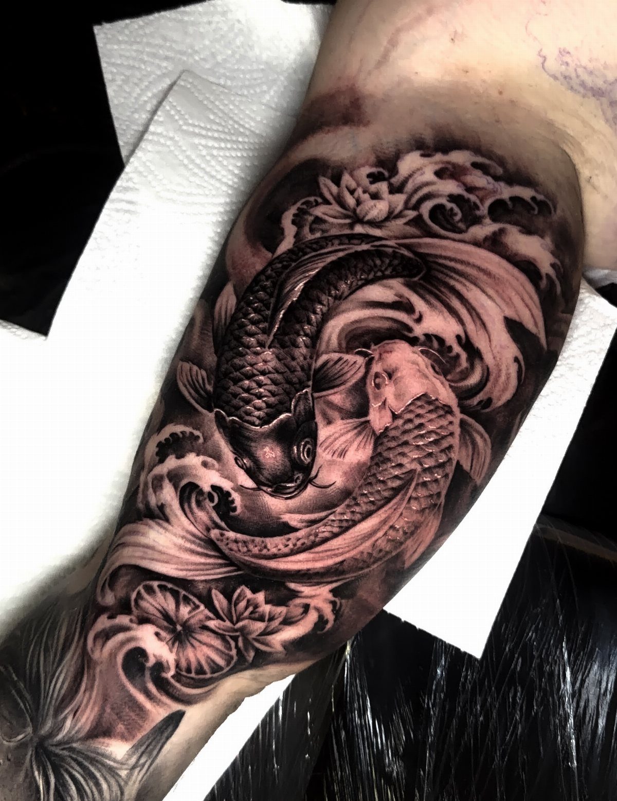 Koi fish tattoo on inner bicep with swirling waves and floral details.