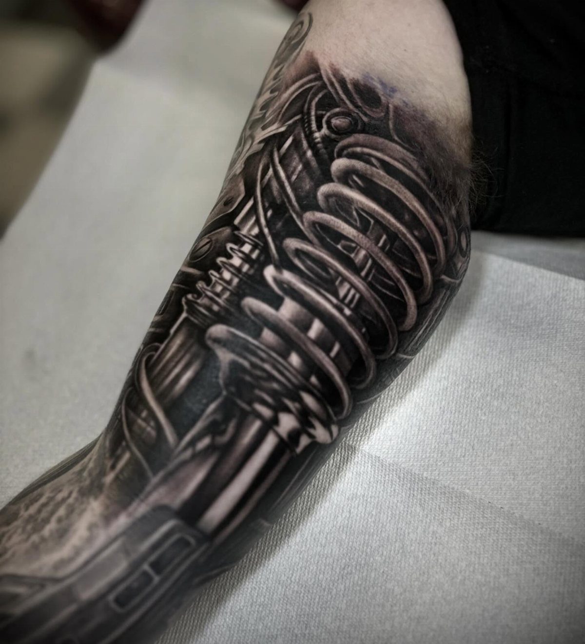 Biomechanical tattoo on an arm showing detailed metallic springs and mechanical parts.