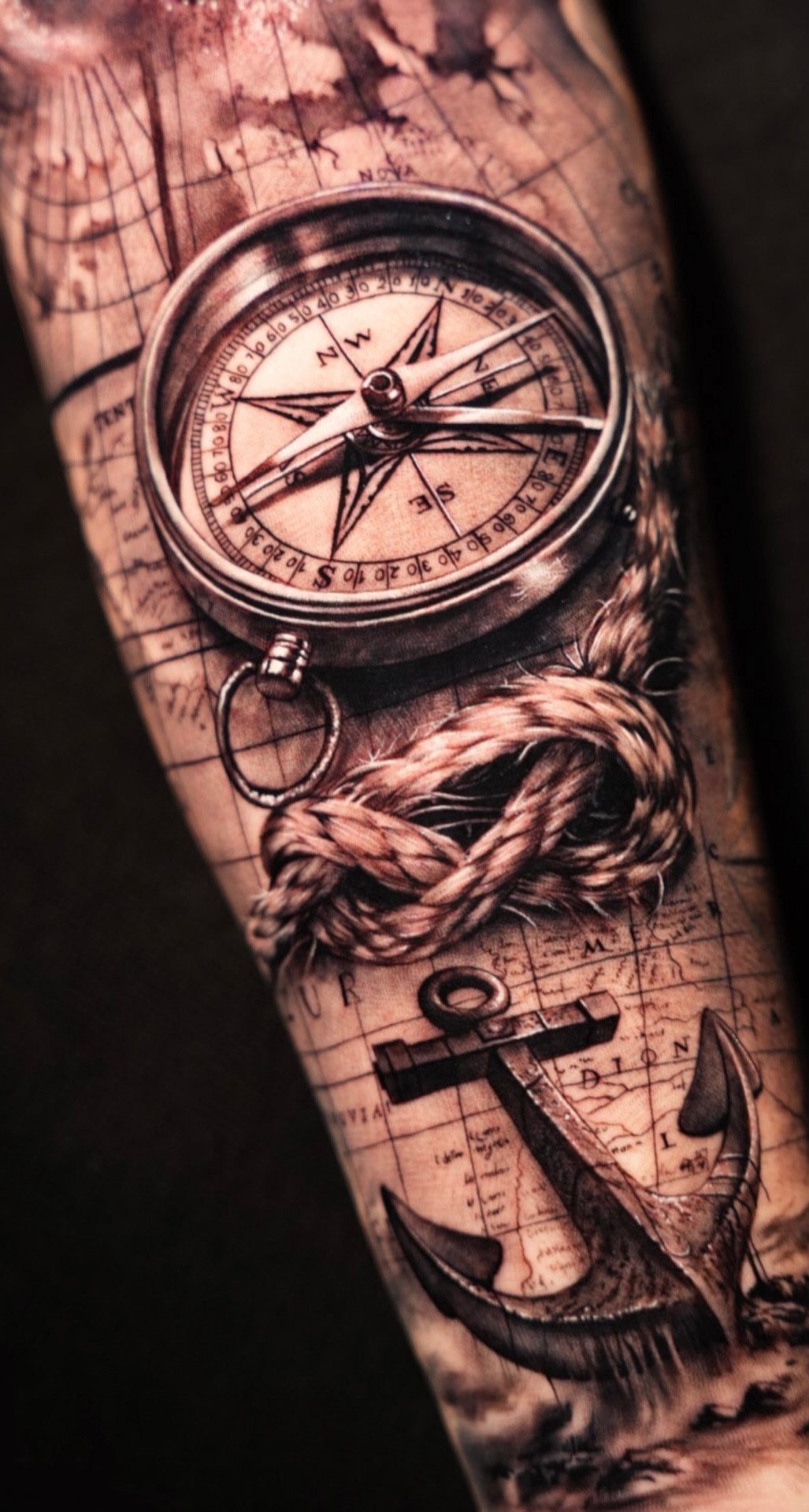 Nautical compass, anchor, and rope tattoo on an arm with map background.