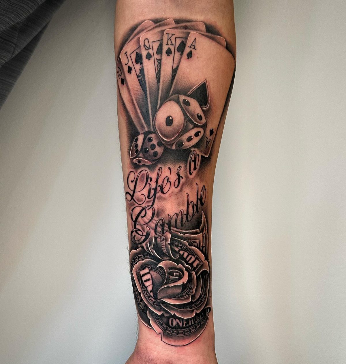 Inner bicep tattoo featuring playing cards, dice, a rose, and gambling quote text.