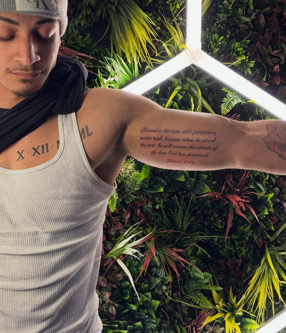 Man showing a cursive quote tattoo on his inner bicep and chest tattoos.