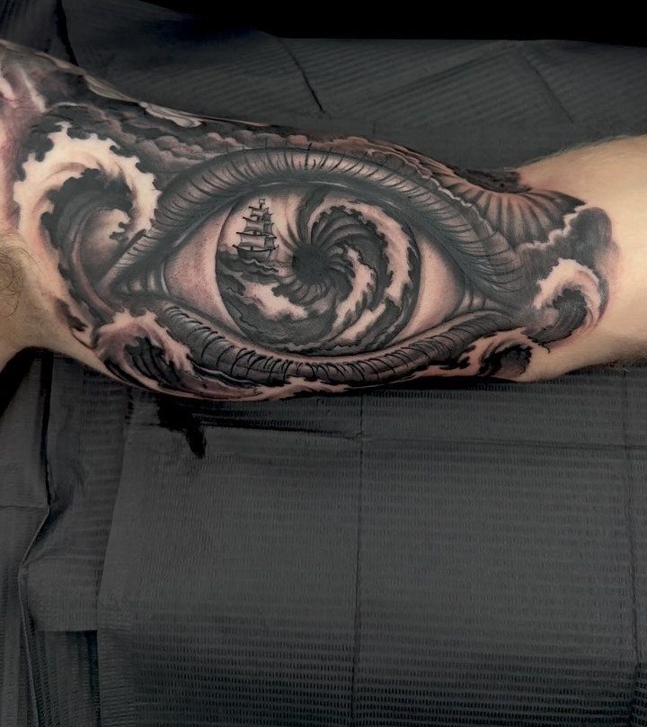 Black and grey inner arm tattoo of an eye containing a stormy ocean vortex.