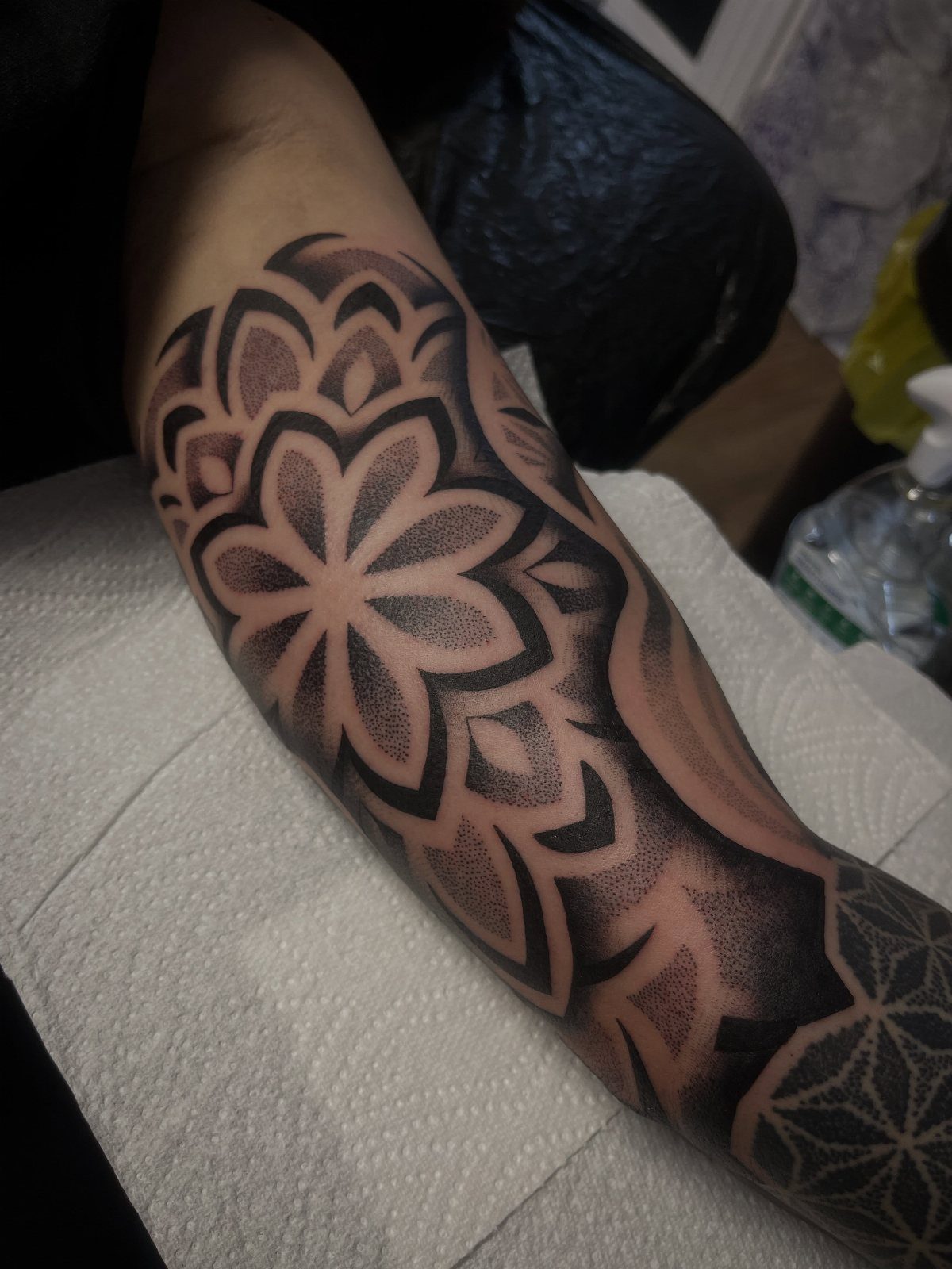 Geometric flower tattoo with symmetrical petals on a person's inner bicep arm.
