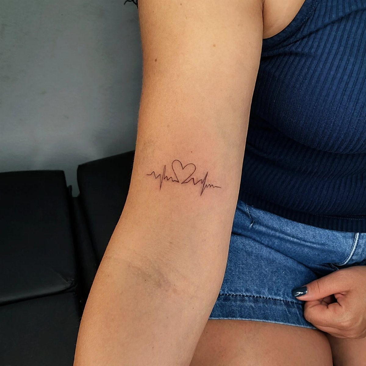 Inner bicep tattoo of a heartbeat line with a heart in the center