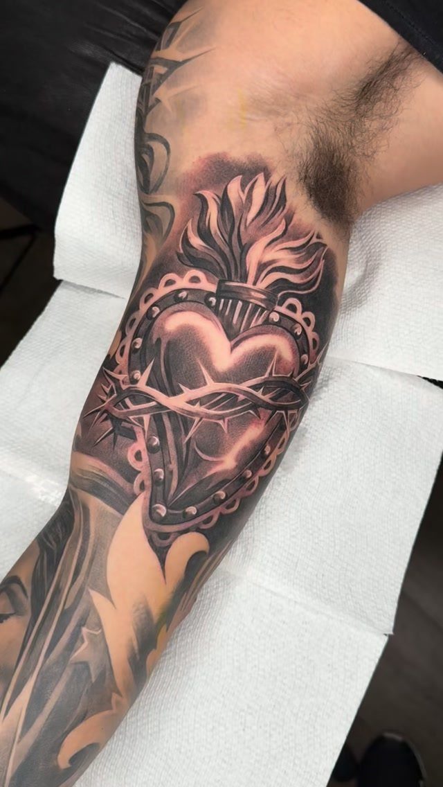 Flaming heart tattoo with crown of thorns on a person's inner bicep.