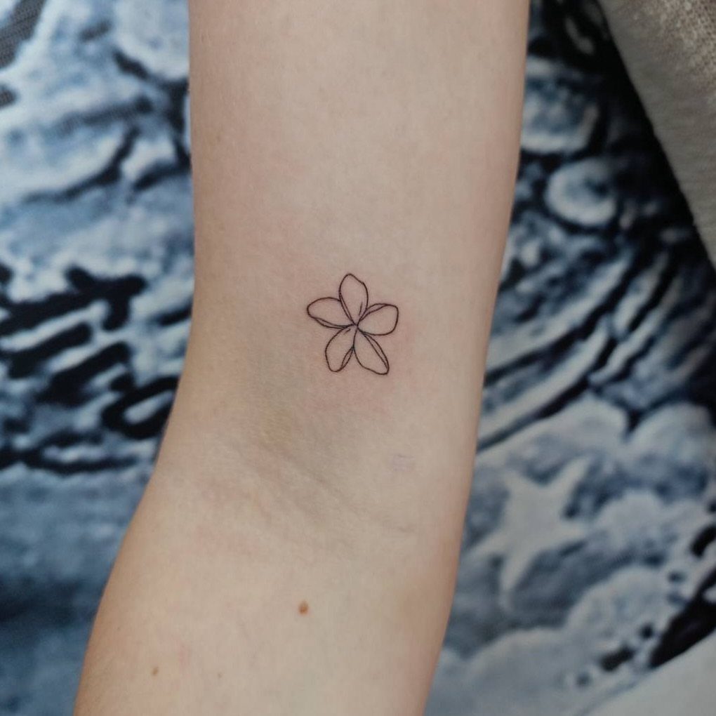 Small black ink flower tattoo on a person's inner forearm