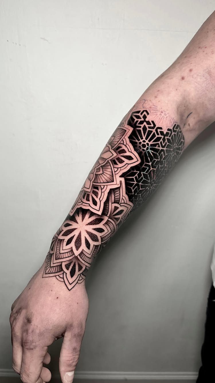 Geometric mandala tattoo with symmetrical patterns on a person's inner forearm.