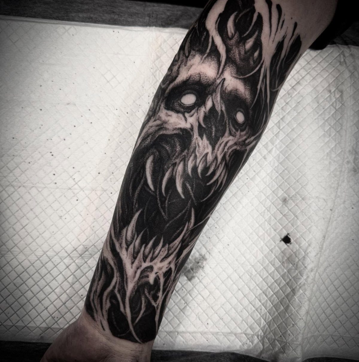 Inner forearm tattoo of a detailed black and grey skull with flame accents.