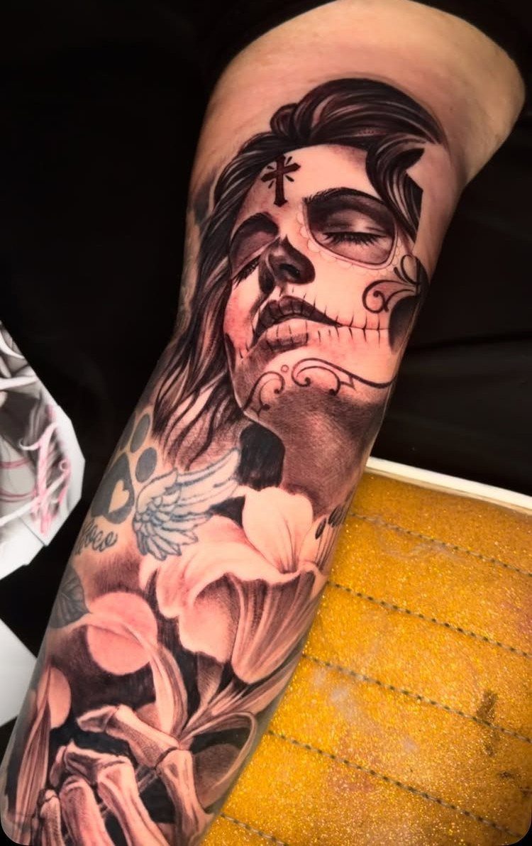 Inner forearm tattoo of a woman with sugar skull makeup and lilies.