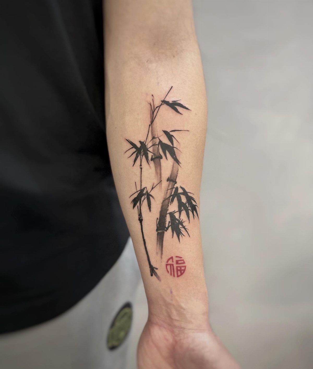 Bamboo tattoo with black ink and a red seal on a forearm